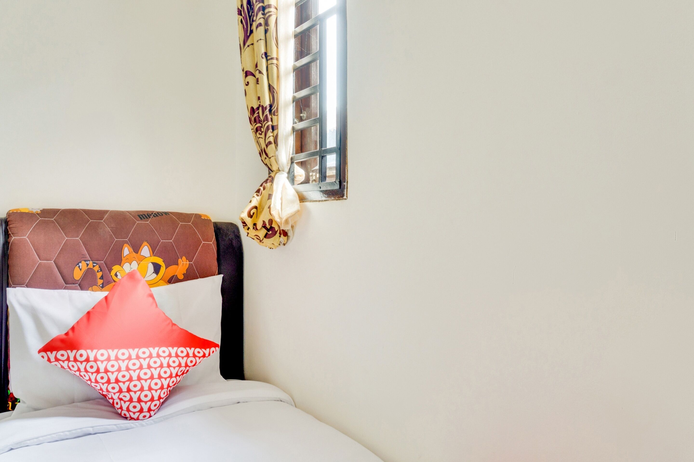 A bed with a patterned pillow, a decorative headboard, and a window with curtains.