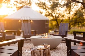A cozy outdoor seating area with a fire pit, lounge chairs, and a rustic wooden table with snacks and drinks.
