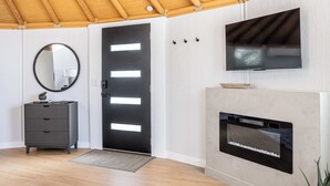 Una habitación moderna con techo de madera, una puerta negra con paneles iluminados, un televisor de pantalla plana montado en la pared y una chimenea con frente de vidrio.