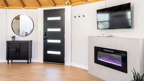 Een moderne woonkamer met een houten plafond, een zwarte deur met verlichte panelen, een ronde spiegel, een flatscreen televisie en een ingebouwde open haard.