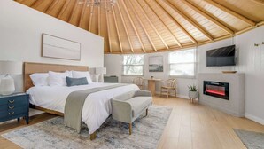 Ein Schlafzimmer mit Holzboden, einem Bett, einem Fernseher, einem Kamin und einem Schreibtisch.