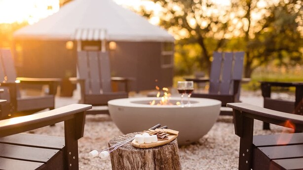 Ein gemütlicher Außenbereich mit Feuerstelle, Lounge-Stühlen und einem rustikalen Holztisch mit Snacks und Getränken.