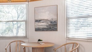 Ein Zimmer mit Holzboden, einem runden Tisch, zwei Holzstühlen und einem Bild an der Wand.