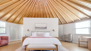 Ein Schlafzimmer mit Holzboden, einem Bett mit weißer Bettwäsche, einer Bank, einem Nachttisch und einem kleinen Schrank.