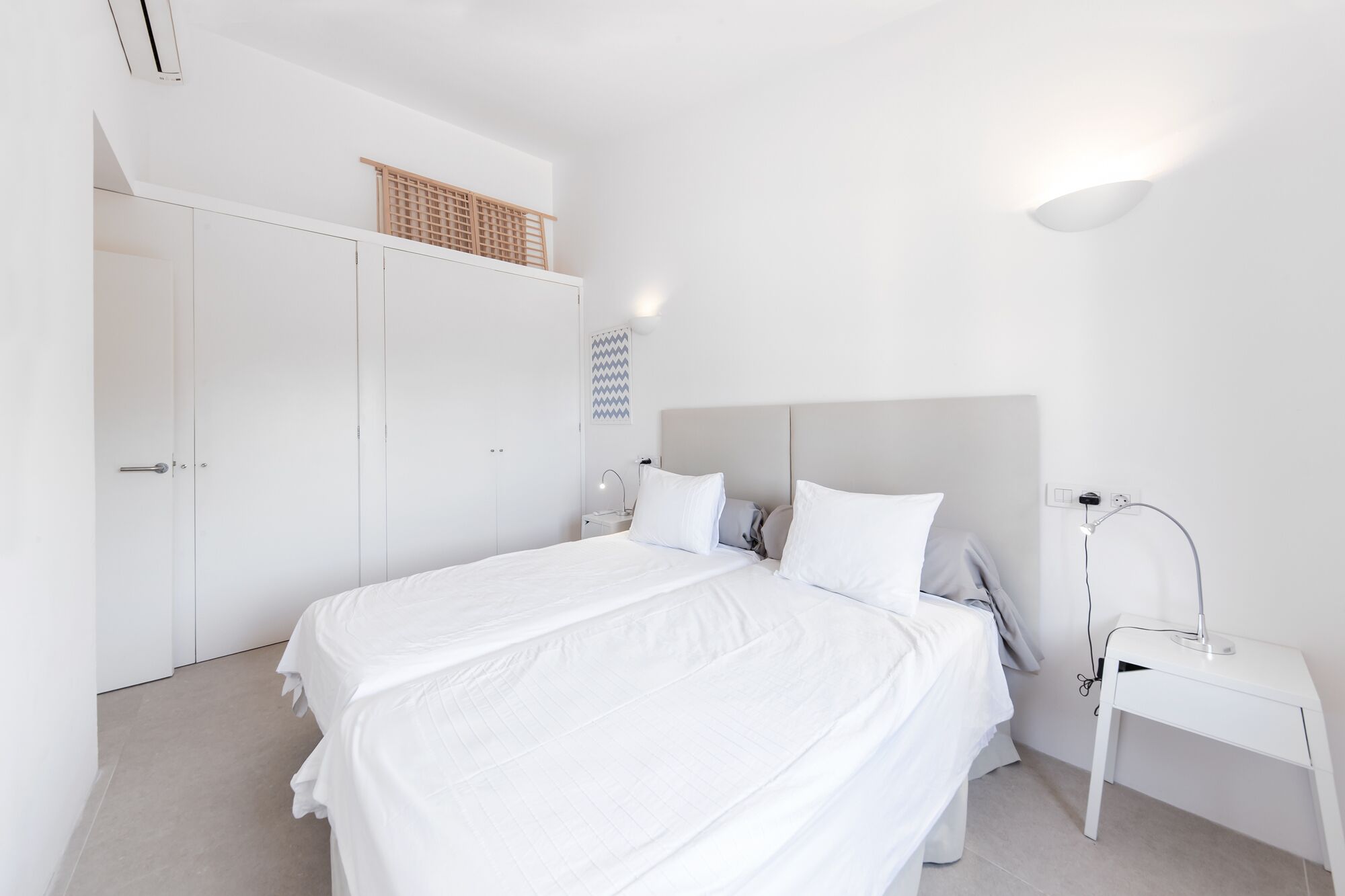 Een minimalistische slaapkamer met een groot bed, een nachtkastje, een lamp en een kledingkast.