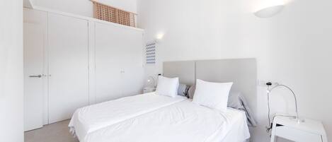 Een minimalistische slaapkamer met een groot bed, een nachtkastje, een lamp en een kledingkast.