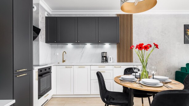 A modern kitchen with dark cabinets, white countertops, and a dining area with a wooden table and black chairs.