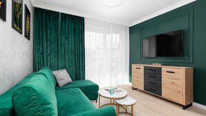 A modern living room with a green sofa, a TV, a wooden cabinet, and a small round table.