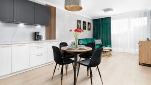 A modern kitchen with white cabinets, a dining area with a round table and chairs, and a green sofa in the living room.