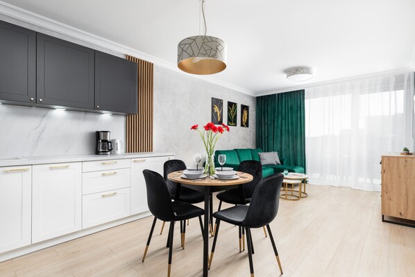A modern kitchen with white cabinets, a dining area with a round table and chairs, and a green sofa in the living room.