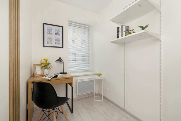 Una habitación pequeña y luminosa con escritorio, silla, radiador y ventana con persianas.
