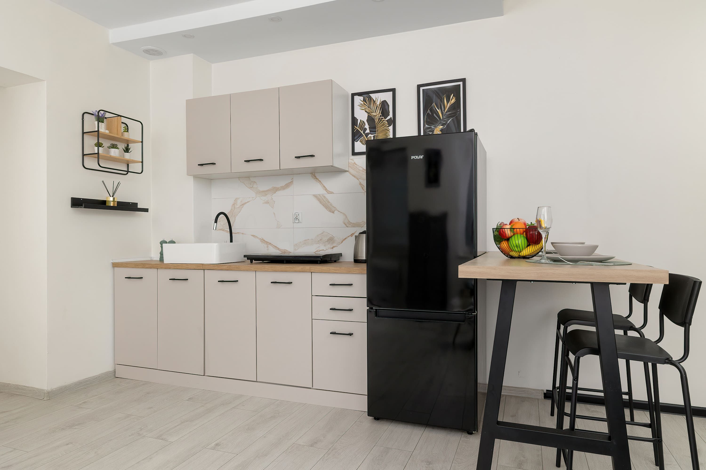 A modern kitchen with a black refrigerator, light-colored cabinets, and a dining area with a table and chairs.