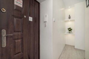 A wooden door with a 'No Smoking' sign, a wall-mounted phone, and a small shelf with a statue and a plant.