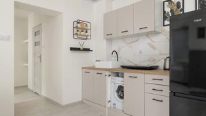 Une cuisine moderne avec des meubles de couleur claire, un réfrigérateur noir, un dosseret en marbre et un lave-linge encastré.