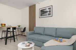 A modern living room with a sofa, a dining table with chairs, a small white table with a candle and a magazine, and a framed picture on the wall. - A bright studio | The perfect space for remote working (Chorzów)