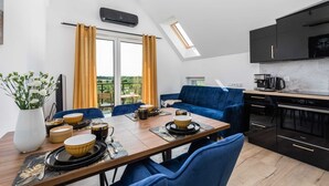 A modern kitchen with black cabinets, a dining area with a blue sofa, and a view of greenery through the window. - Stylish Apartment | Parking, Balcony, Close to the Beach (Sianozety)