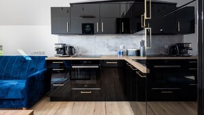 A modern kitchen with black cabinets, a marble countertop, and a blue sofa. - Stylish Apartment | Parking, Balcony, Close to the Beach (Sianozety)