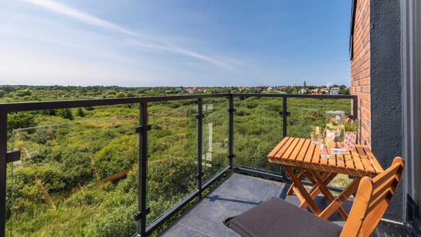 A balcony with a wooden table and chairs, offering a view of a green landscape. - Stylish Apartment | Parking, Balcony, Close to the Beach (Sianozety)