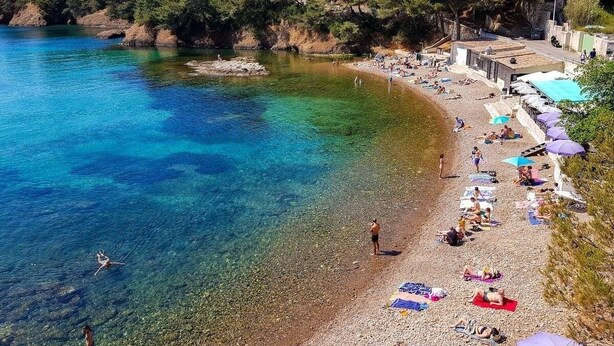 Una spiaggia con acqua cristallina, persone che prendono il sole e ombrelloni.