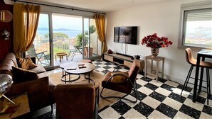 Un soggiorno con pavimento a scacchi, un divano, un tavolino da caffè, una televisione e un balcone con vista.