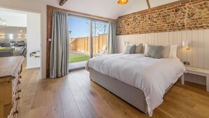 Un dormitorio con una cama grande, piso de madera, pared de piedra y puerta corredera de vidrio que da a un patio.