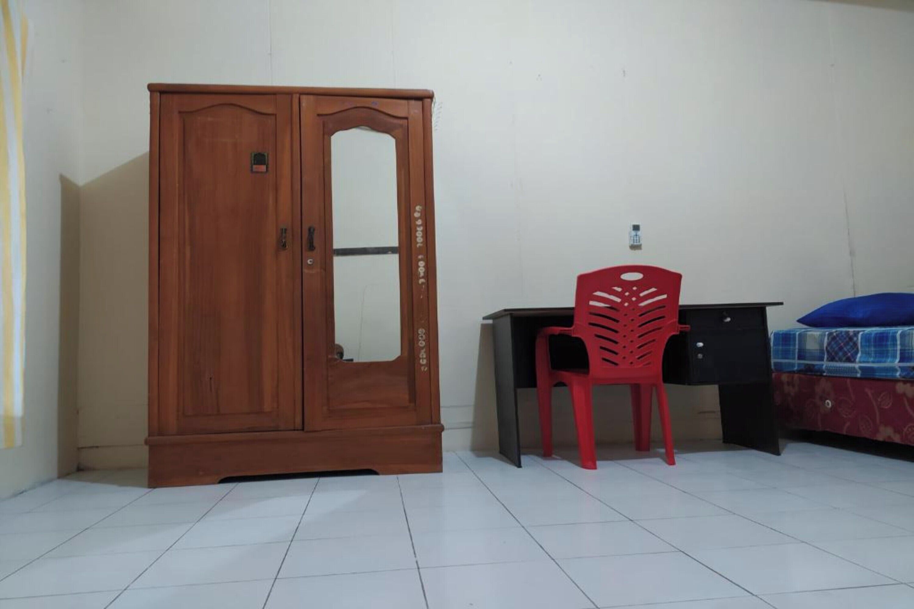 Una stanza con un'armadio in legno, una scrivania con una sedia rossa e un letto con copriletto a motivi blu e bianchi.