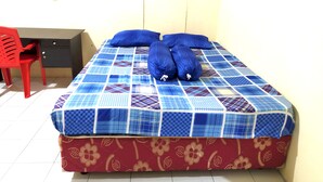 A bed with a blue and red patterned bedspread, two pillows, and a red chair. - Hotel O Batu Putih Homestay (Makassar)