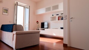 A modern living room with a sofa, a TV, and a kitchen area with cabinets and a door. - Marechiare Intera in Ortona (Ortona)