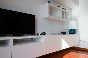 Una sala moderna con un televisor de pantalla plana sobre un mueble blanco, una lámpara y un cuenco decorativo azul.
