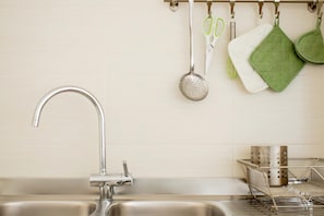 A kitchen with a stainless steel sink, a metal strainer, green and white kitchen towels, and a metal colander.
