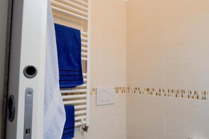 Ein Badezimmer mit weißen Fliesen, einem weißen Heizkörper und einem Handtuchhalter mit blauen Handtüchern.