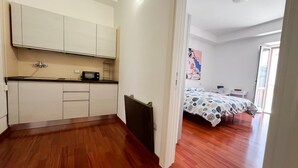 A compact room with a kitchenette, a bed with a patterned bedspread, and a door leading to another room. - Marechiare Intera in Ortona (Ortona)