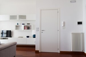 Una sala moderna con televisor de pantalla plana, un sofá, una puerta blanca y un radiador.