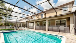 Une piscine entourée de parois en verre, des chaises longues et un espace patio couvert.