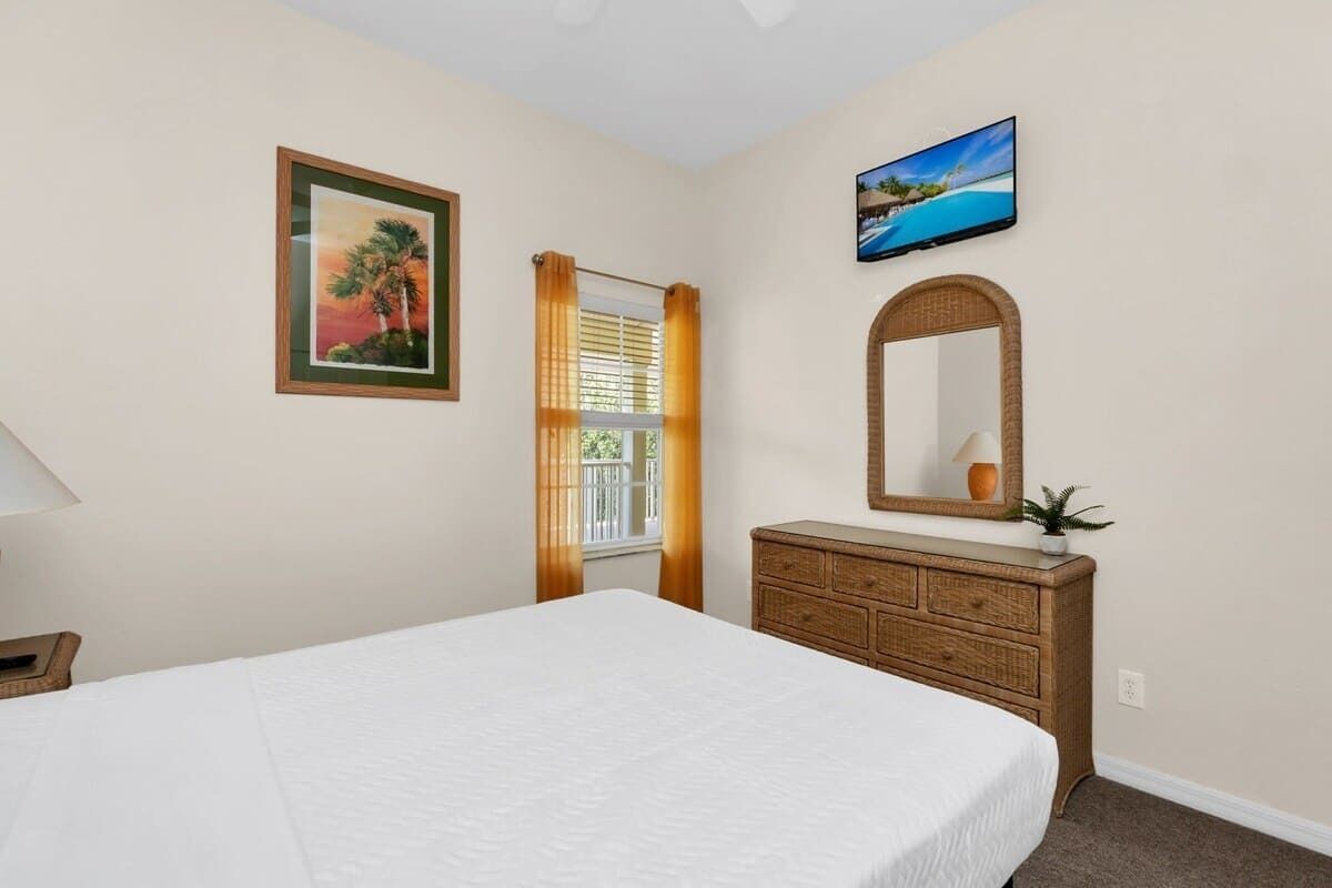 A bedroom with a bed, a dresser, a mirror, a television, and a window with curtains.