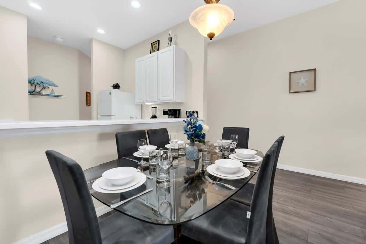 A dining area with a glass table, black chairs, white plates, and a vase of flowers.