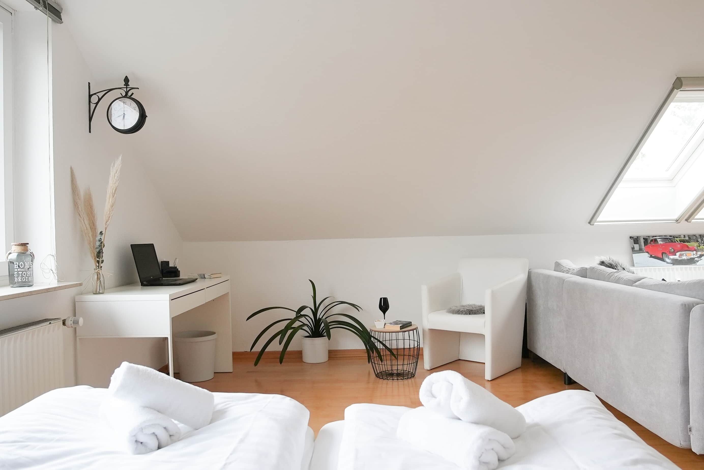 A modern, well-lit room with a white desk, a comfortable sofa, and a bed with white linens.