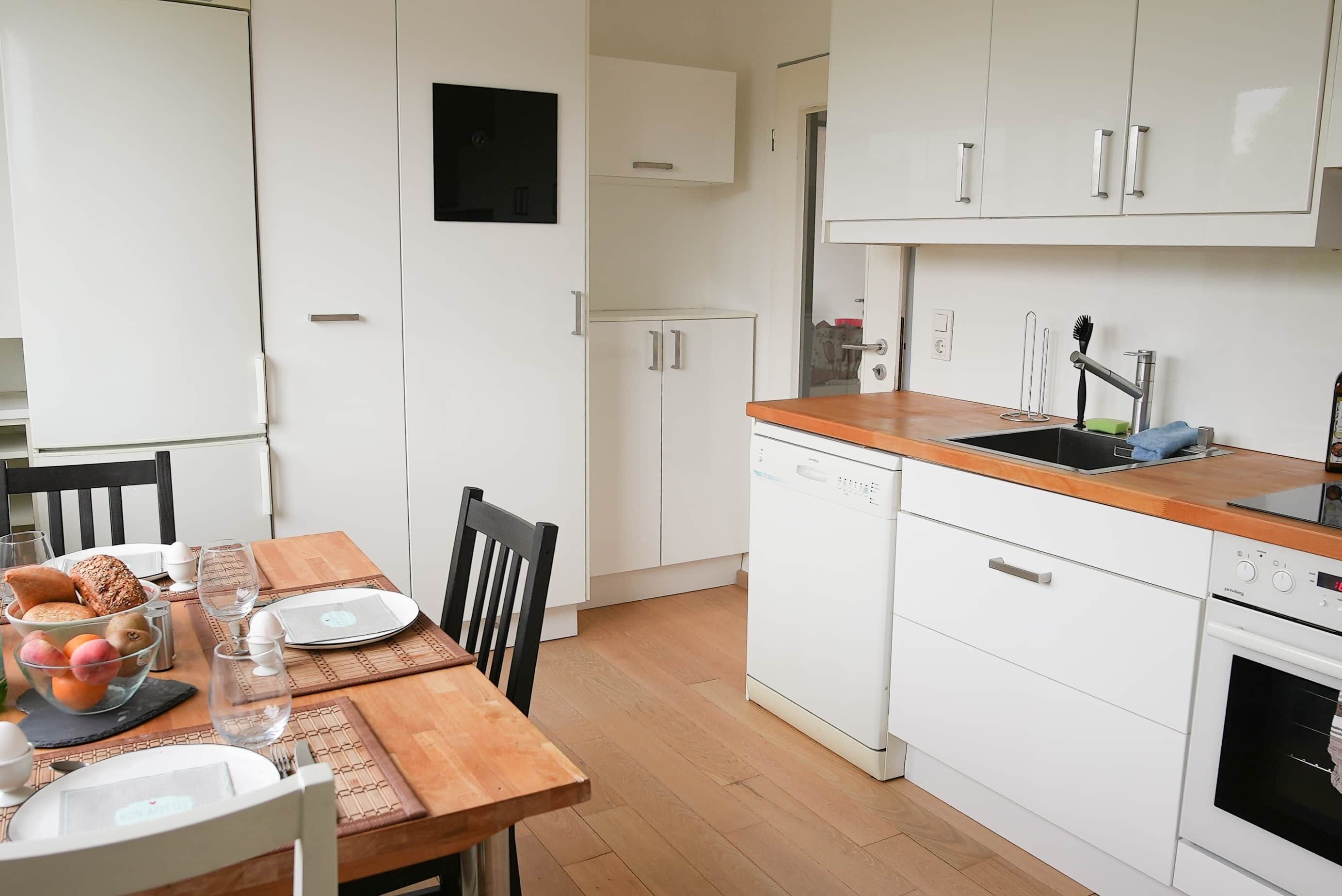 Una cocina compacta con armarios blancos, encimera de madera y lavavajillas.