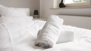 Una cama bien hecha con sábanas blancas y dos toallas enrolladas sobre ella.