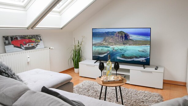 Una sala de estar moderna con tragaluces, un televisor de pantalla plana, un mueble blanco para entretenimiento y una zona de estar acogedora.