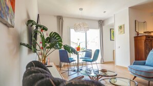 Uma sala de estar moderna com área de jantar, destacando uma planta grande, cadeiras azuis e uma mesa de centro de vidro.