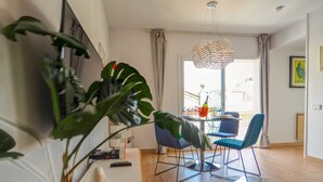 Uma sala de estar moderna com uma mesa de jantar de vidro, cadeiras azuis e uma planta grande.