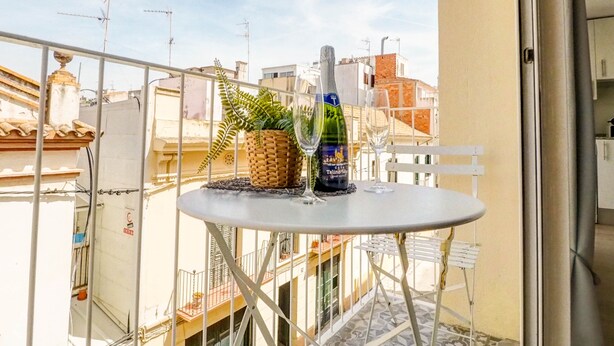 Uma varanda com mesa, uma garrafa de vinho e um copo, com vista para a paisagem urbana.