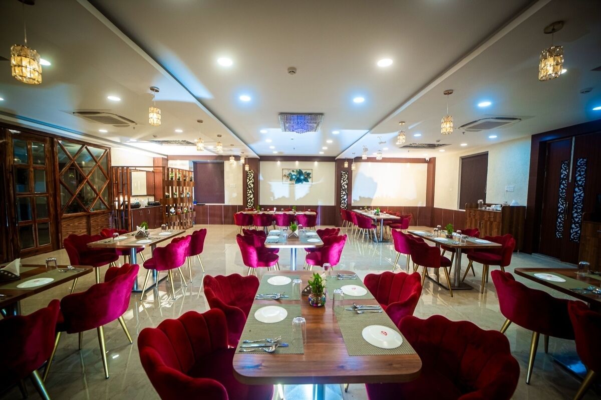Un vaste espace dédié à la salle à manger, avec plusieurs tables et des chaises rouges, agrémenté d’un design moderne au niveau du plafond et de meubles de rangement en bois.