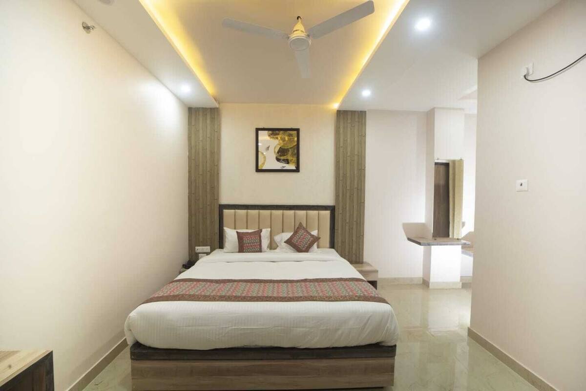 A modern hotel room with a large bed, a ceiling fan, recessed lighting, and a bathroom visible through an open door.