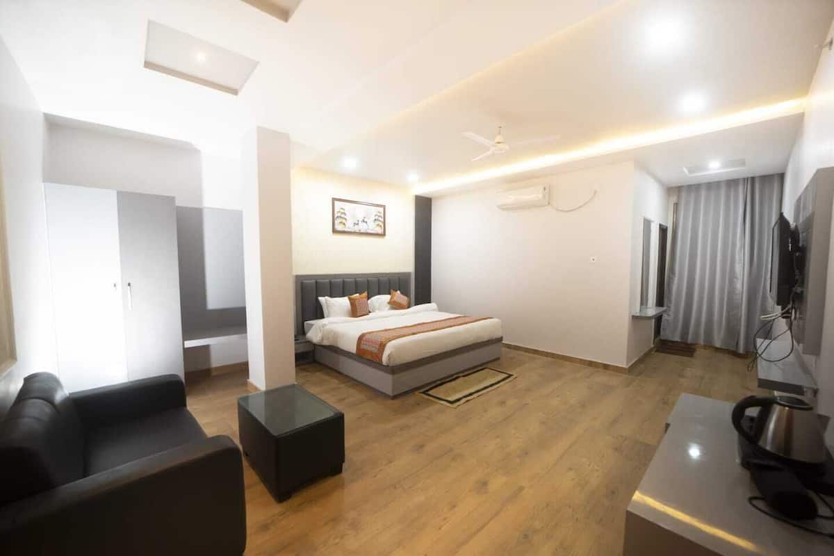 A modern hotel room with a large bed, a sofa, a desk, and a ceiling fan.