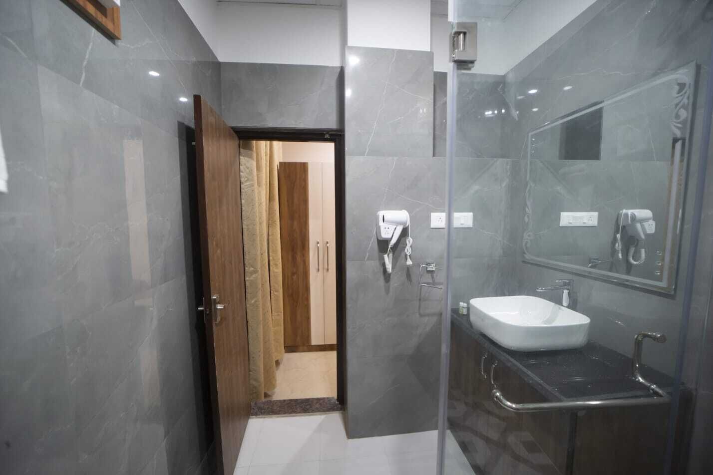 Un baño moderno con cabina de ducha de vidrio, un lavabo blanco y una puerta de madera que da a otra habitación.