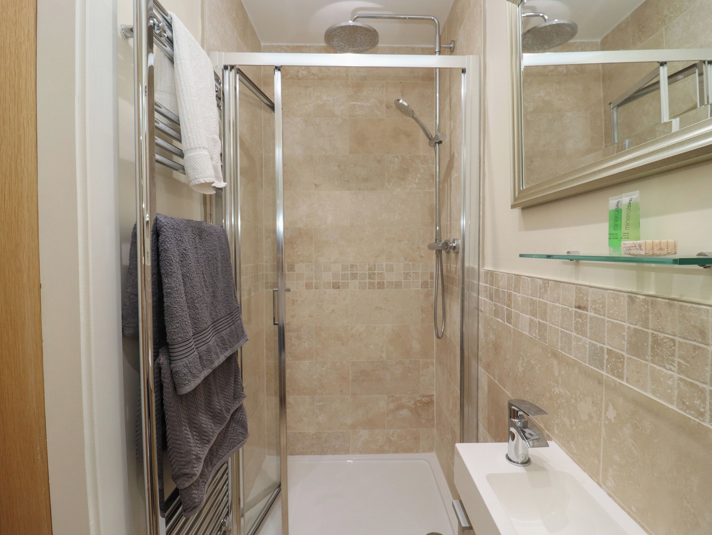 Une salle de bain moderne avec une douche à parois de verre, un lavabo blanc et un miroir au-dessus du lavabo.