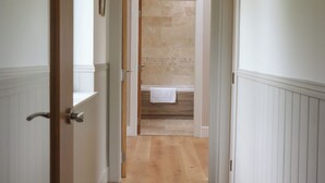 A hallway leading to a bathroom with a tiled wall and a wooden floor. - Cotswold View (Witney)
