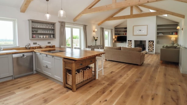 A spacious kitchen with wooden beams, a central island, and a dining area with a sofa. - Cotswold View (Witney)